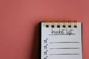 Top view image of notebook with text BUCKET LIST on pink background.